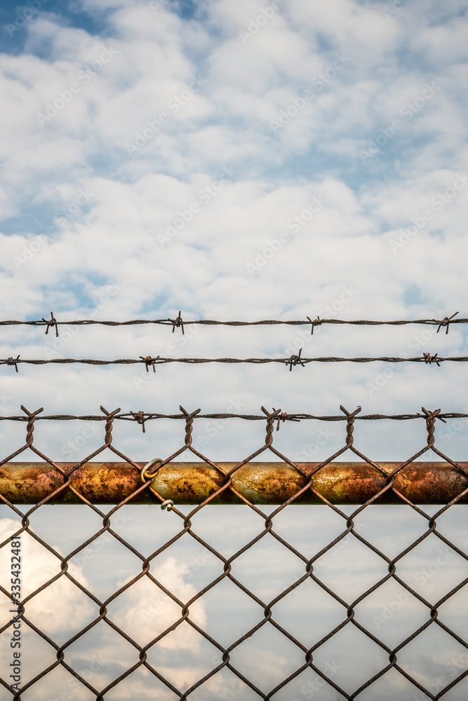 A rusty chain link fence topped with barbed wire. Selective focus - soft focus background A rusty chain link fence topped with barbed wire. Selective focus - soft focus background