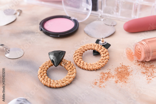 Earrings with makeup cosmetics on grey background