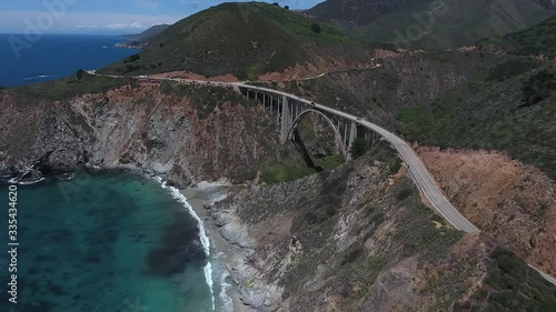 Aerial of Bixby Creek Bridge traffic with canyon cliffs on the blue water off the coast of Big Sur California