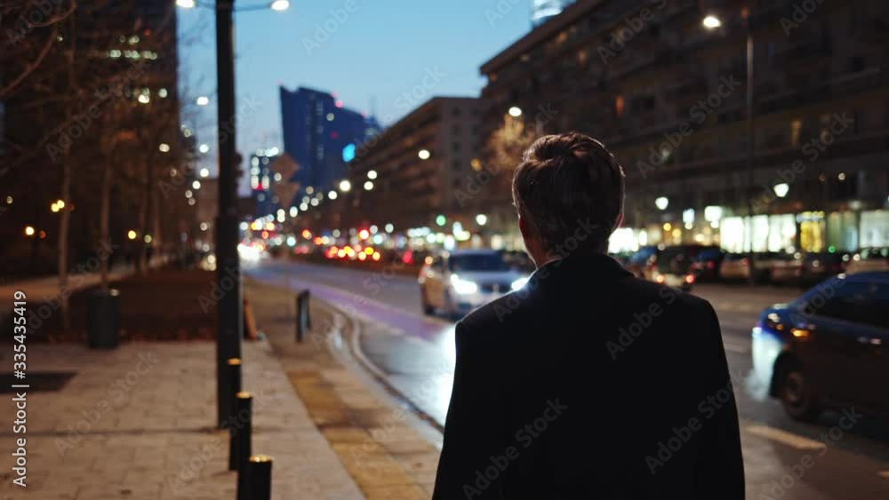 Businessman in black coat walks on modern town street at evening time. Following caucasian mature man traveling around city center. Urban life concept. Businessman in black coat walks on modern town street at evening time. Following caucasian mature man traveling around city center. Urban life concept.
