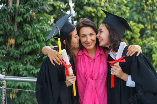 Middle aged Caucasian mom is being kissed by graduated daughter and her friend.