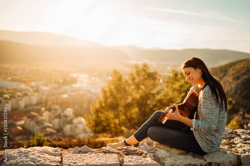 Young guitarist playing acoustic guitar and looking to sunset.Searching inspiration.Music creator.New artist in good mood.Musical talent.Smiling young woman singing and playing acoustic guitar.