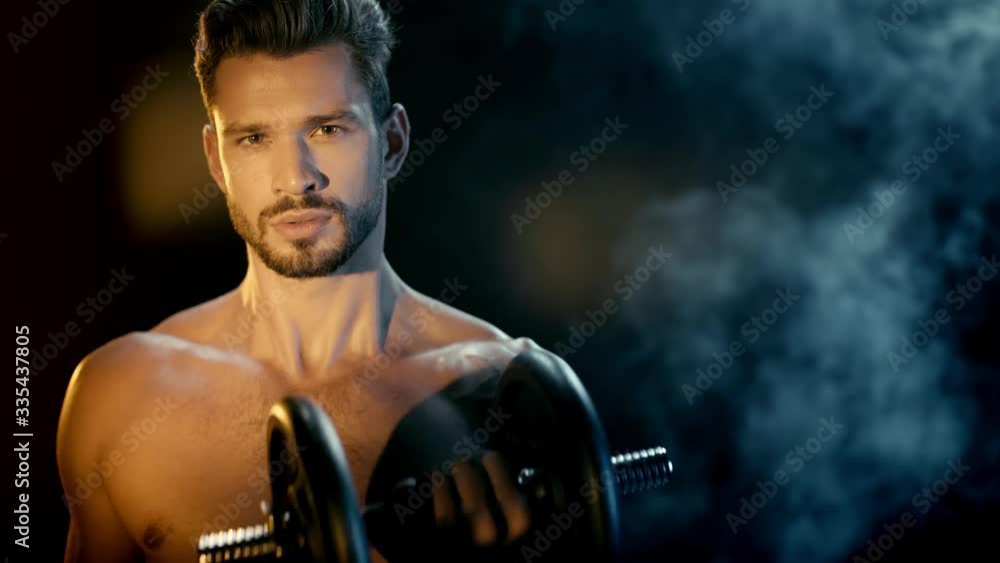 Sportsman raising dumbbell and looking at camera with smoke behind on black Sportsman raising dumbbell and looking at camera with smoke behind on black