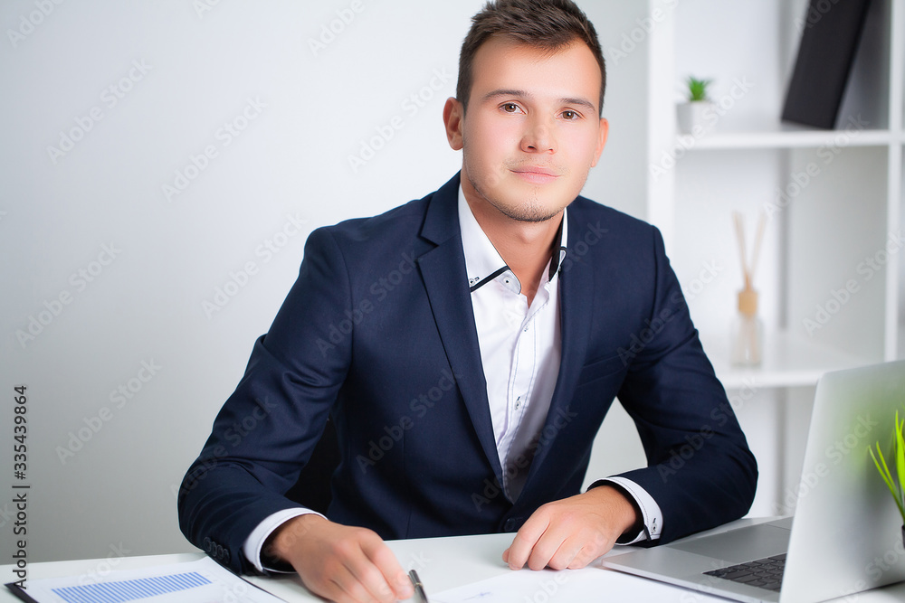 Handsome young worker working in a company office with documents and a laptop Handsome young worker working in a company office with documents and a laptop