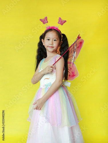 Beautiful asian little girl dressed in fairy costume isolated over yellow background.