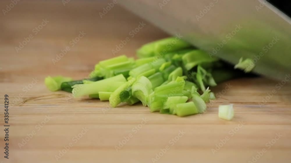 The cook cuts green onions with a sharp knife on a cutting board The cook cuts green onions with a sharp knife on a cutting board