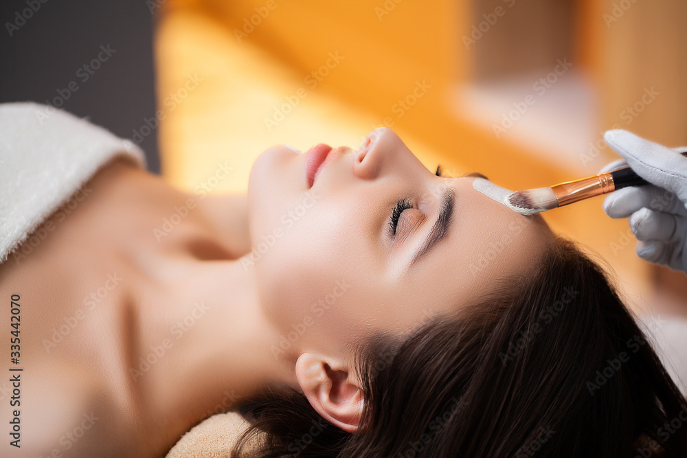 Fototapeta premium Pretty woman applying face mask at spa salon