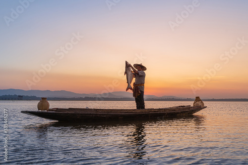 Picture of Asian fishermen on a wooden boat Thai fishermen catch fresh water fish in the natural river, traditional Thai fishermen at the morning sun on the lake of Thailand