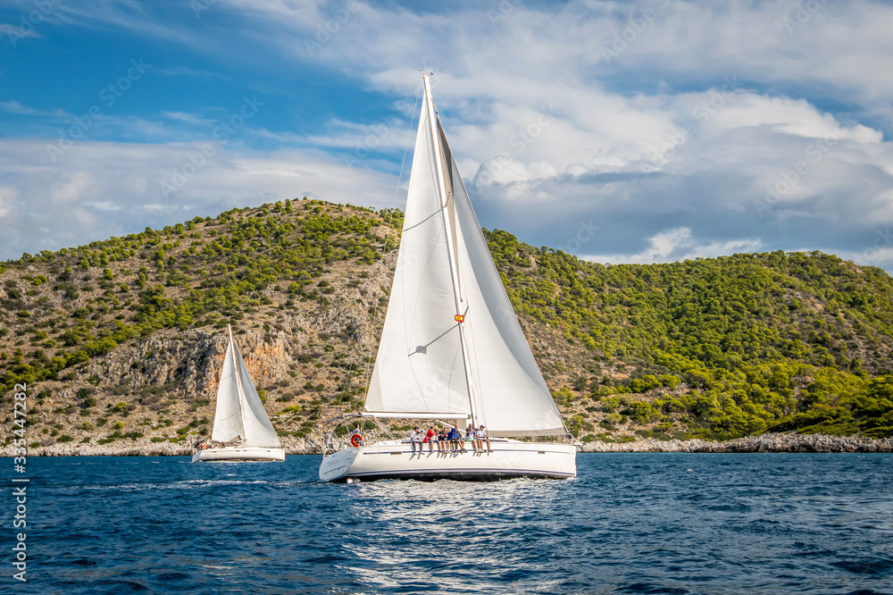 Obraz premium two sailing yachts with white sails floating on the sea among the rocks