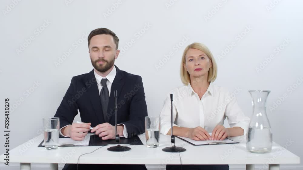 Male and female company representatives sitting at desk in studio and listening to questions while holding press conference Male and female company representatives sitting at desk in studio and listening to questions while holding press conference