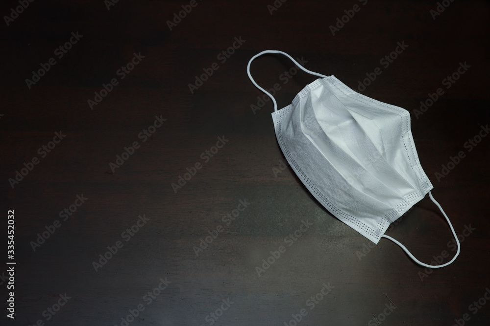 A surgical face mask or protective mask on a dark black wooden table in the background. Virus spread protection concept. A surgical face mask or protective mask on a dark black wooden table in the background. Virus spread protection concept.