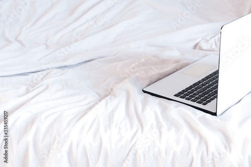 home office in a bed. white and black laptop on white crumpled sheets