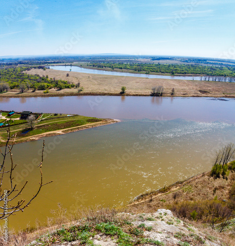 Fototapeta Naklejka Na Ścianę i Meble -  Top view of the bend of the river, two banks, bare branches against the blue sky on a spring day
