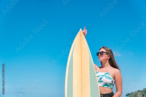 Rear view of beautiful asian young surfer girl with surfboard on a beach. Woman runs into the ocean with surfboard. Sporty people having fun in sunny day - Extreme sport, travel and vacation concept.