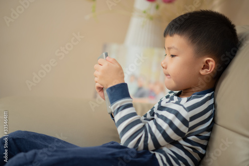 Asian child (boy) at home during Covid-19 lockdown, playing with smartphone