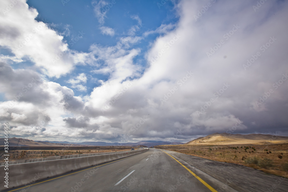 Asphalt road and bright blue sky with fluffy clouds . Empty desert asphalt road from low angle with mountains and clouds on background. road, red desert landscape . Open road with blue clouds .