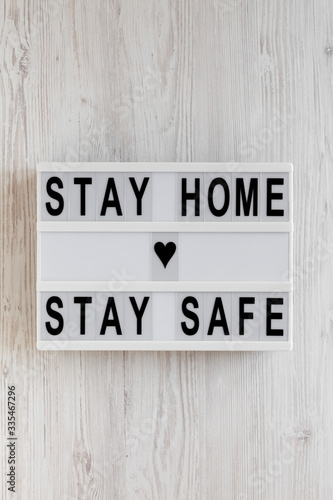 'Stay home stay safe' words on a lightbox on a white wooden background, top view. Overhead, from above, flat lay.