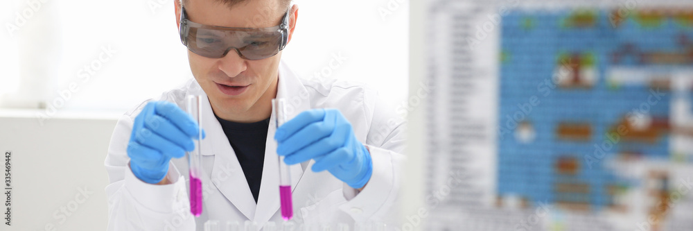 A male chemist holds test tube of glass in his hand overflows a liquid solution of potassium permanganate conducts an analysis reaction takes various versions of reagents using chemical manufacturing