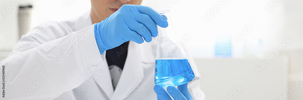 A male chemist holds test tube of glass in his hand overflows a liquid solution of potassium permanganate conducts an analysis reaction takes various versions of reagents using chemical manufacturing A male chemist holds test tube of glass in his hand overflows a liquid solution of potassium permanganate conducts an analysis reaction takes various versions of reagents using chemical manufacturing