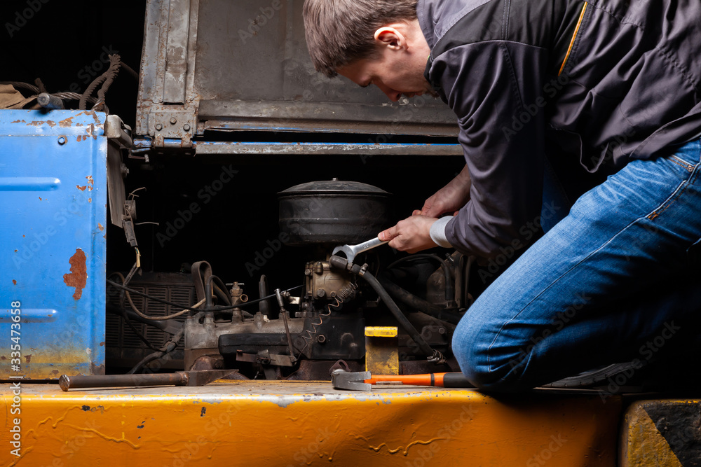 A male mechanic is repairing the engine of an old truck with an open hood with a wrench. Auto service industry.