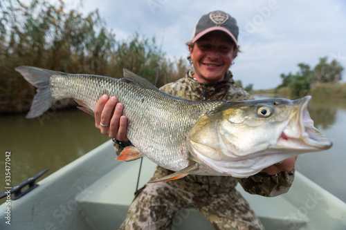 Angler sits in the boat and holds the trophy Asp fish