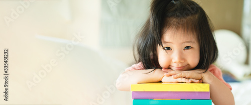 Photo Panoramic portrait of Asian girl toddler smiling put her chin over her hands on the books stack
