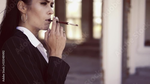 camera move from female hand with cigarette holder to face woman in suit smoke outdoors