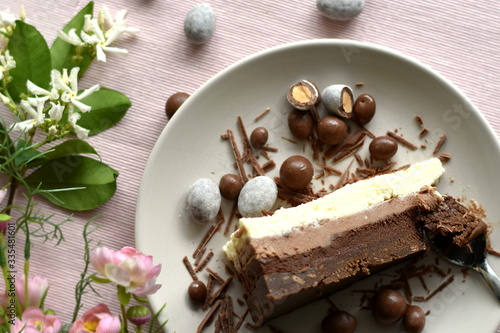 Slice of raw ketogenic cake with three different chocolate layers on a plate  decorated with confetti and flowers. Healthy diet concept. Pink wedding concept. Selective focus  shallow dof. Top view.