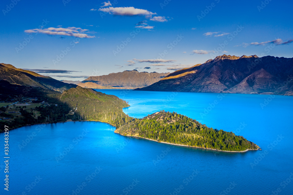 Green lush Forest peninsula on Lake Wakatipo with Southern Alps mountains in the background, aerial view at sunset
