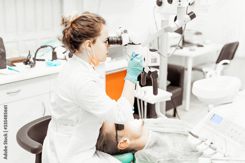 Dentist young woman treats a patient a man. The doctor uses disposable gloves, a mask and a hat. The dentist works in the patient's mouth, uses a professional tool. Dentist young woman treats a patient a man. The doctor uses disposable gloves, a mask and a hat. The dentist works in the patient's mouth, uses a professional tool.