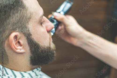 Beauty shop for men. Shaving a beard in a barbershop. Barber cuts his beard with a razor and clipper. close up Brutal haircuts. Hairdresser equipment. Selective focus.