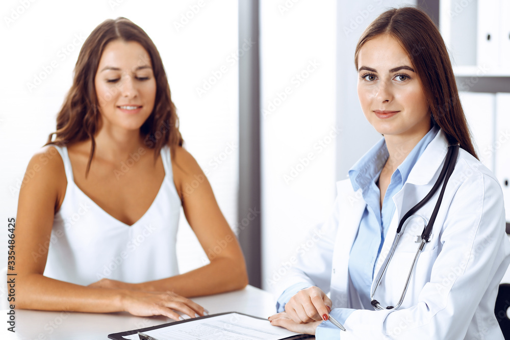 Doctor and happy patient talking while sitting at the desk. The physician or therapist discussing healthy lifestyle. Health care, medicine and patient service concept Doctor and happy patient talking while sitting at the desk. The physician or therapist discussing healthy lifestyle. Health care, medicine and patient service concept