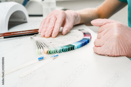 Manicurist at work in the office. Drawing gel polish on tips, creating a picture. Equipment and inventory of a manicure cabinet.