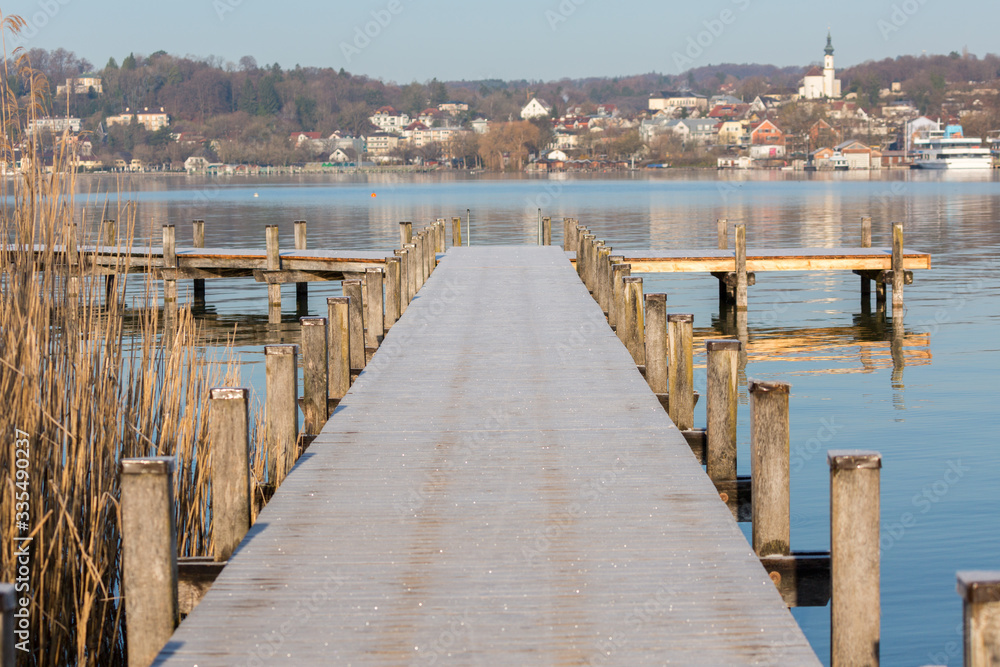 Starnberg, Bavaria / Germany - Mar 31 2020: View along an empty jetty at Lake Starnberg (Starnberger See). The surface of the pier is covered with frost. In the background the town of Starnberg.
