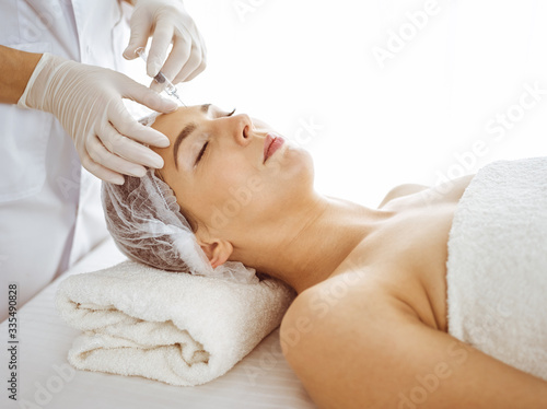 Beautician doing beauty procedure with syringe to face of young brunette woman. Cosmetic medicine and surgery, beauty injections