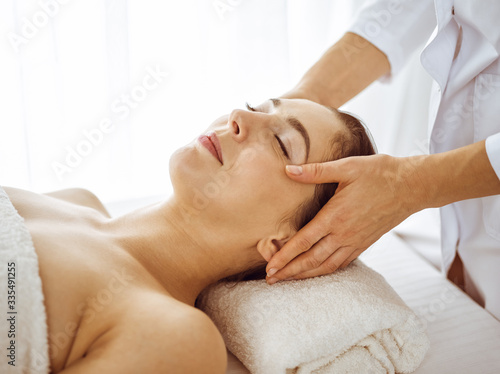 Beautiful brunette woman enjoying facial massage with closed eyes. Relaxing treatment in medicine and spa center concepts