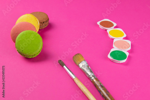 Makarons on a pink background are next to the colors of macaroons and brushes for drawing photo