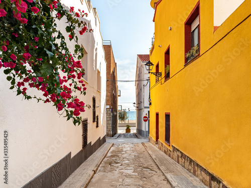 The street leading to the beach and the sea in Masnou port town. A yellow and white building on the sides with red flowers hanging from the wall. El Masnou, Barcelona, Catalunya, Spain. photo