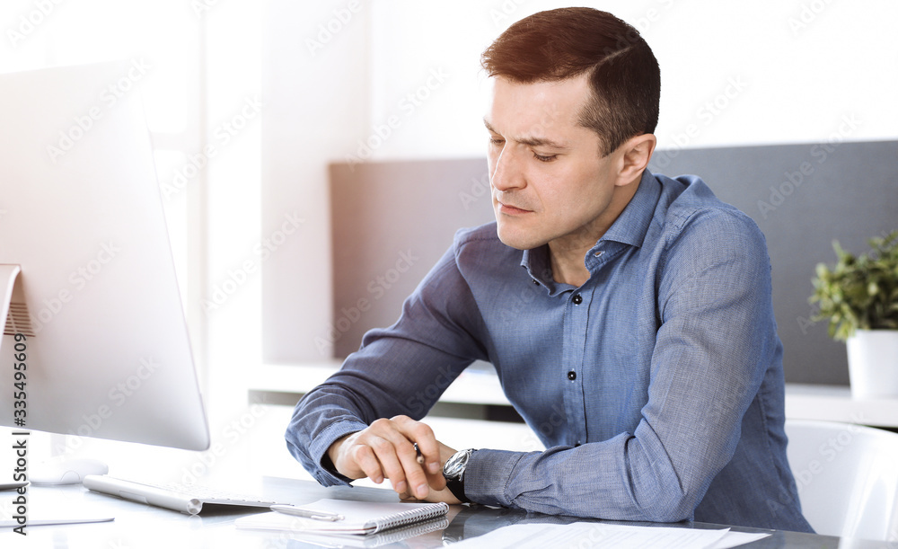Businessman working with computer in modern sunny office. Headshot of male entrepreneur or company director at workplace. Business concept Businessman working with computer in modern sunny office. Headshot of male entrepreneur or company director at workplace. Business concept