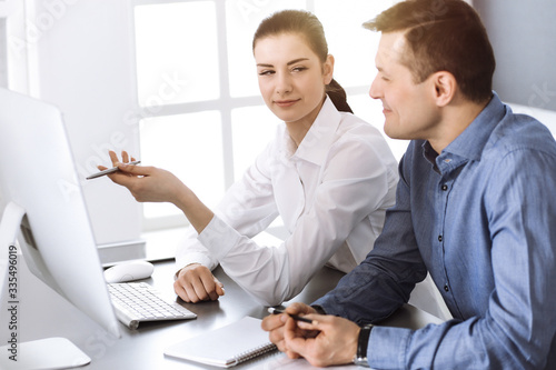 Friendly smiling businessman and woman working with computer in modern office. Headshot at meeting or workplace. Teamwork, partnership and business concept © rogerphoto