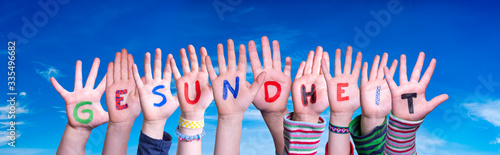 Kids Hands Holding Colorful German Word Gesundheit Means Health. Blue Sky As Background photo