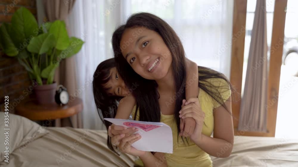 sibling giving surprised love card to her older sister at home sibling giving surprised love card to her older sister at home
