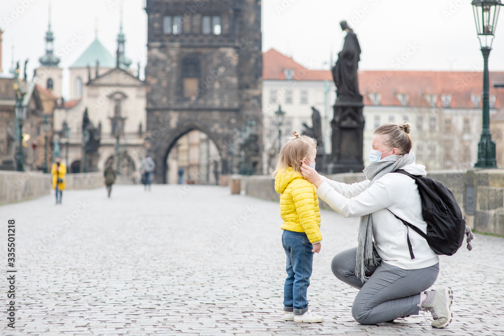 Woman puts on her little daughter a medical mask on Charles Bridge in Prague. Coronavirus epidemic concept. Empty space for text