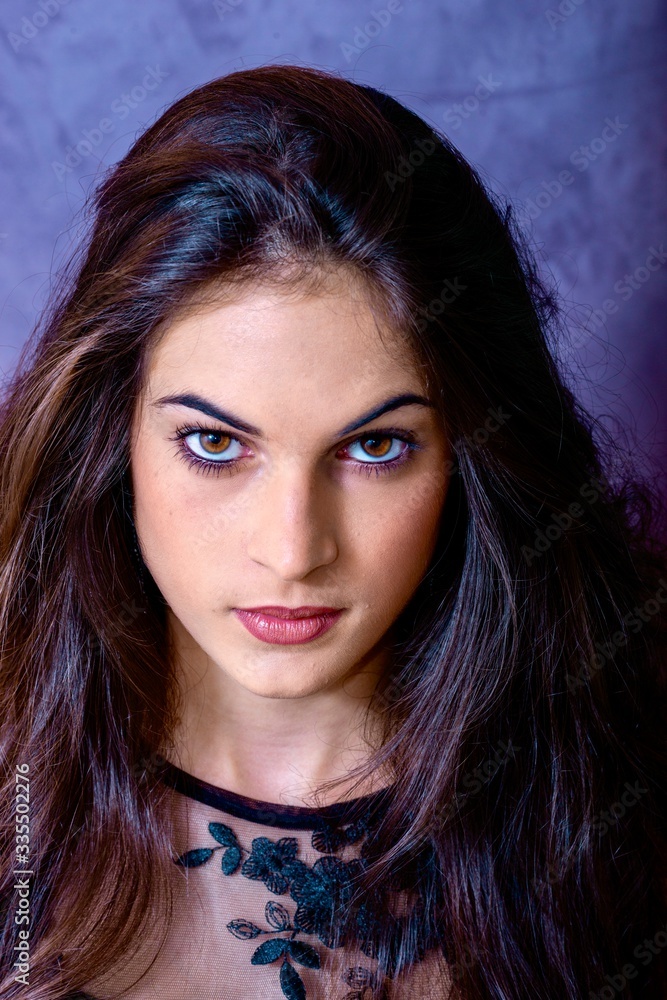 Naklejka premium black hair woman portrait with brown eyes on a gray background , Caucasian ethnic group is looking into the camera with a serious expression on her face. White girl with long black hair and brown eye