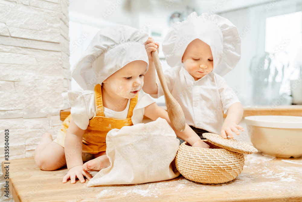 Cute funny restless positive caucasian grimy kids are making pies on a kitchen table. Concept of cute little kids with the desire to learn and practice
