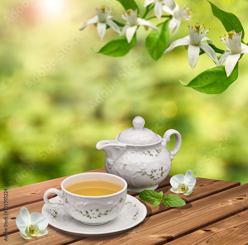 Cup of green tea and teapot on wooden table at garden on green trees background