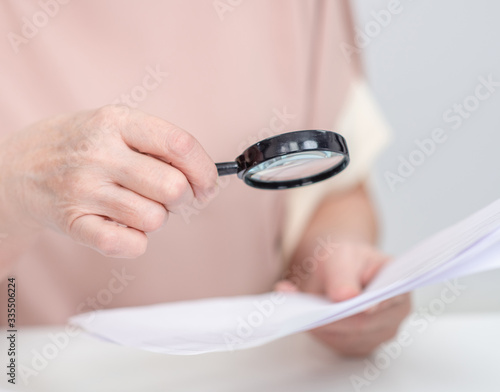 Close up old woman uses a magnifying glass to read a document