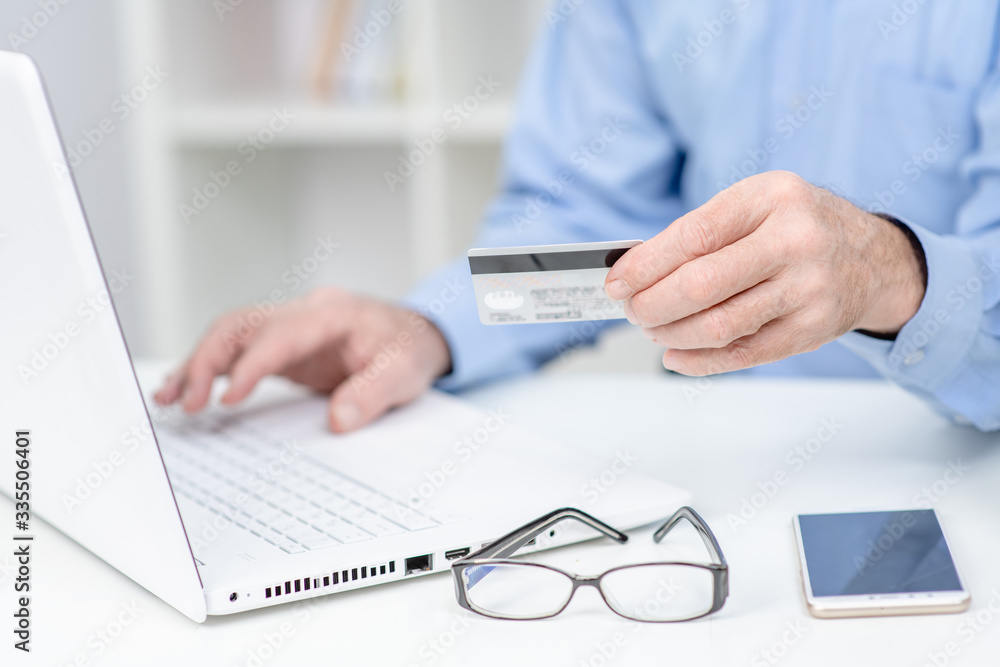Fototapeta premium Hands of an elderly person hold credit card and use laptop. Online shopping