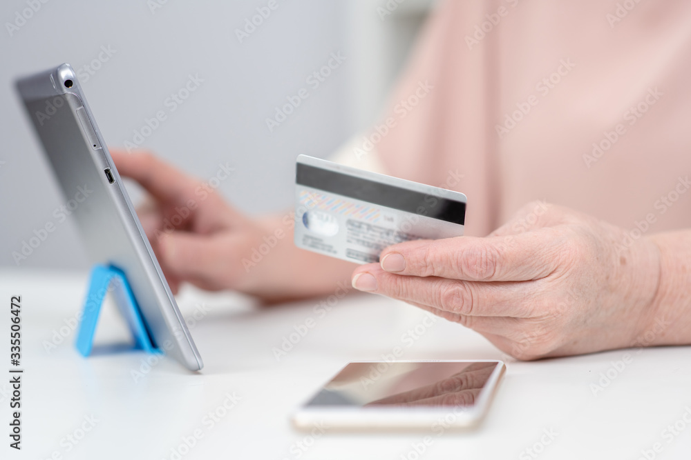 Close up hands of an elderly woman hold credit card and use tablet computer. Online shopping Close up hands of an elderly woman hold credit card and use tablet computer. Online shopping