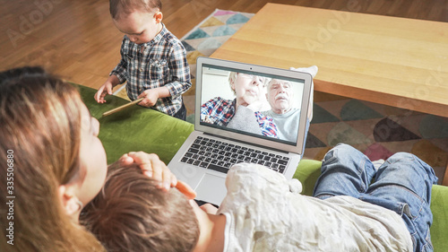 Young mom with two sons having a facetime video call with elderly grandparents. Family connecting with their parents on webcam. Modern technology connecting people of all ages concept.